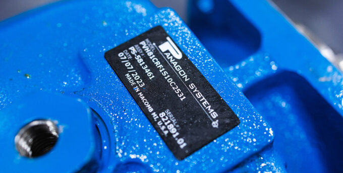 A tag for a piston pump manufactured by Panagon Systems. The tag features the model number, assembly number, date of manufacture, and a serial number and feature the words "Made in Macomb, MI USA"